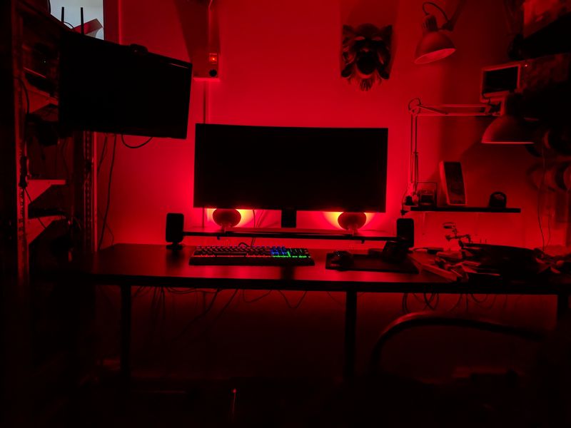 Computer desk with red bias lighting behind ultrawide monitor