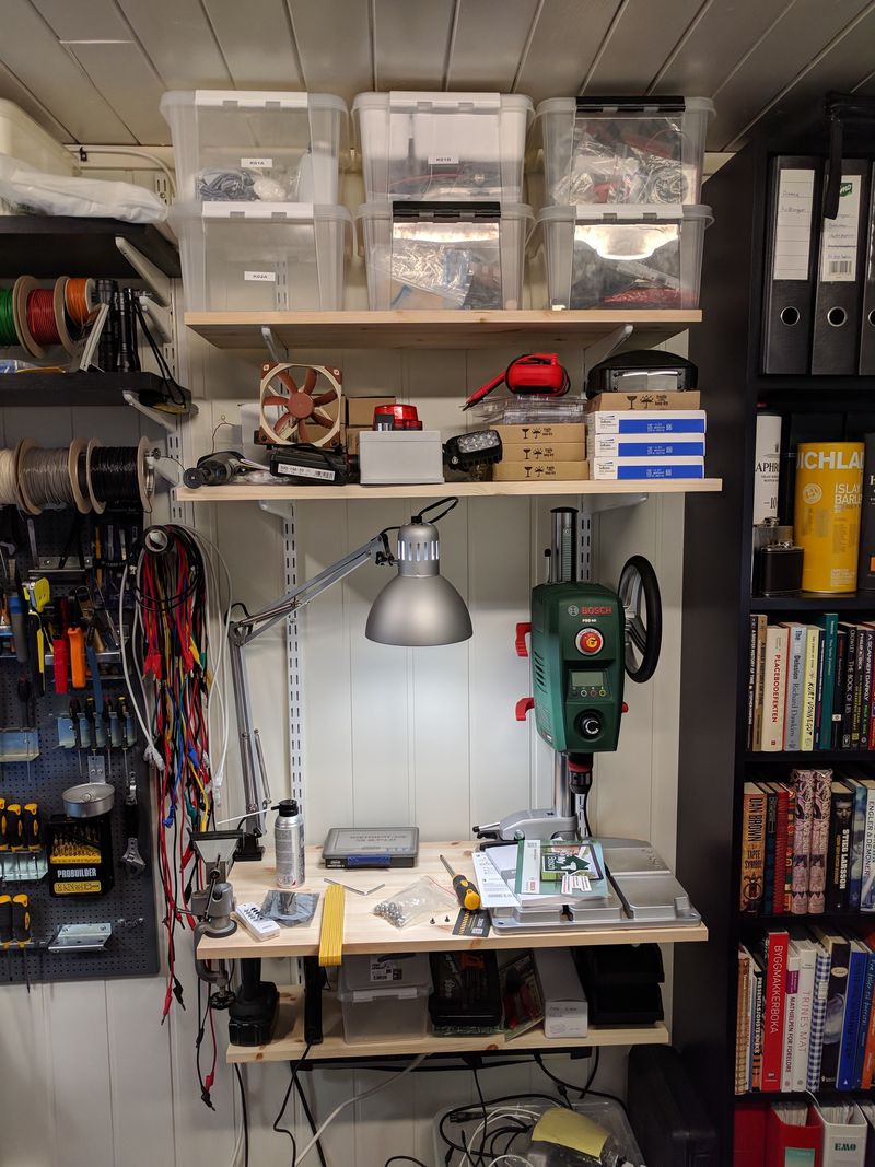 Workbench with shelves, drill press, part storage, and a bit of mess