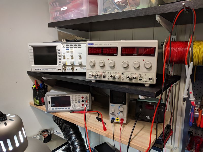 Shelves with an oscilloscope, lab power supplies, multimeter, and a soldering station